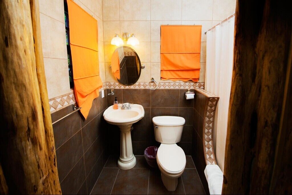 Une salle de bain avec un lavabo sur colonne, des toilettes et un miroir avec éclairage intégré.