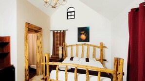 A rustic wooden bed in a room with a sloped ceiling, a small window, and a painting on the wall. - El Gran Mestizo Resort (Orange Walk)