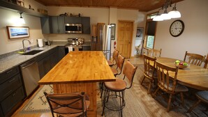 Une cuisine dotée d’un îlot central en bois, de meubles de rangement sombres, d’appareils électroménagers en acier inoxydable et d’un coin repas avec des chaises et une table en bois.