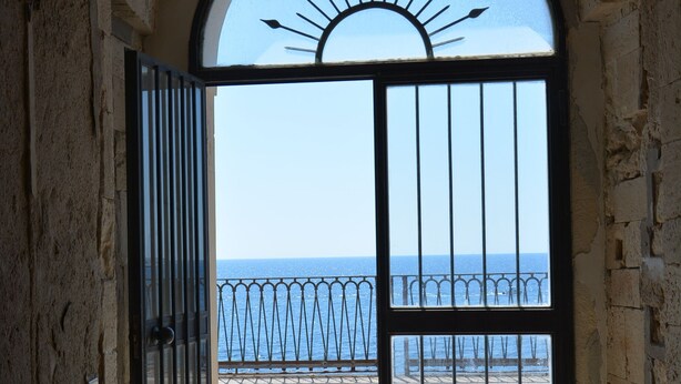 Une porte en arc donnant sur un balcon doté d’une balustrade en métal, d’où l’on peut admirer la mer.