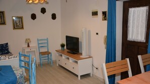 Un salon avec un téléviseur, une table à manger, des chaises bleues et un meuble blanc.