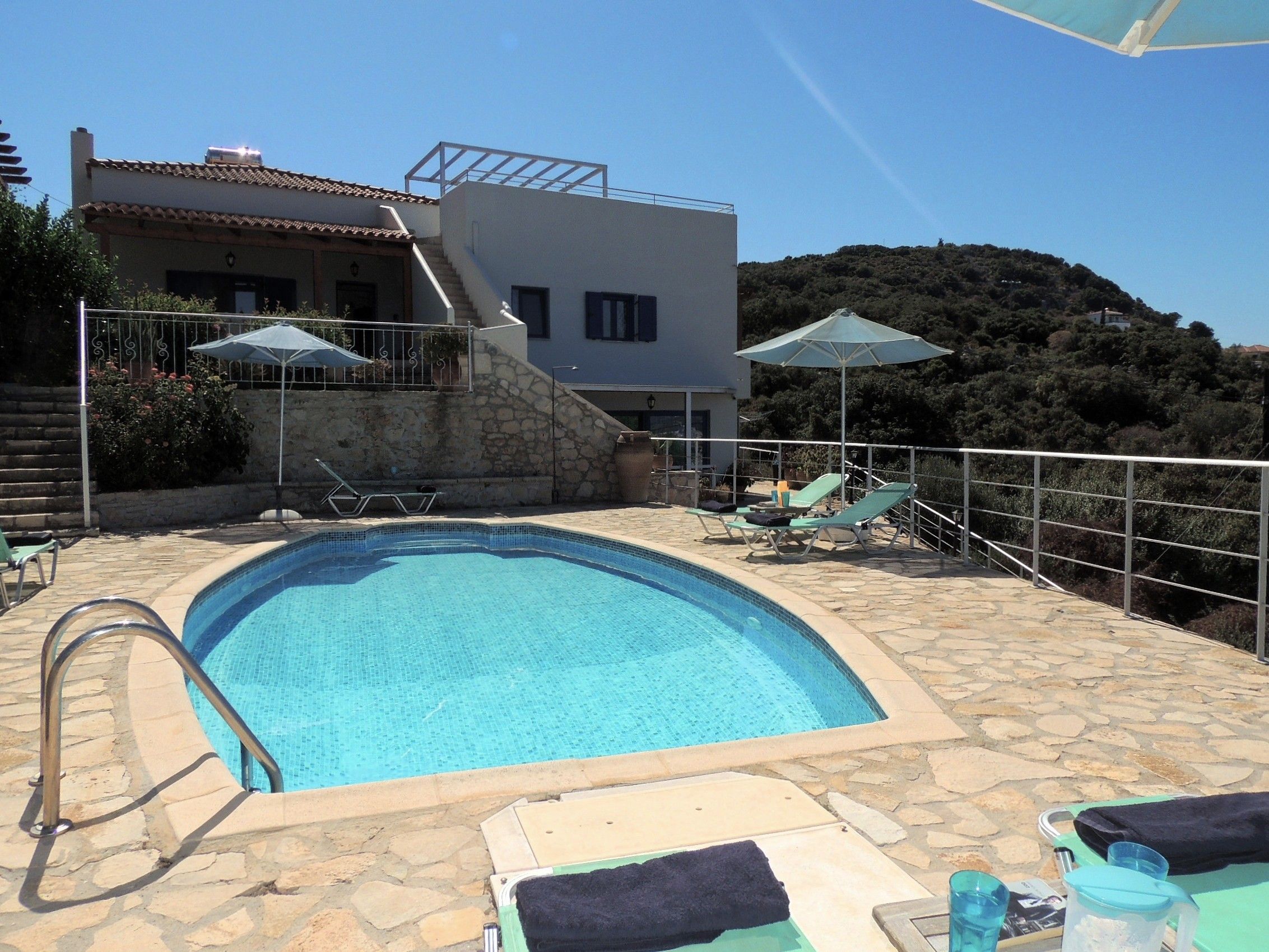 Una piscina con cubierta de piedra, sillas de descanso y sombrillas.
