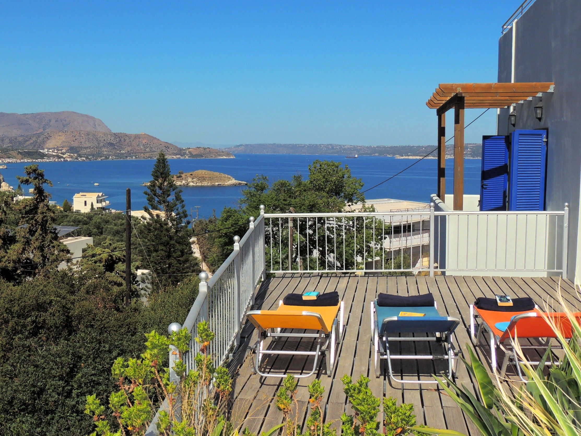 A balcony with a view of the sea, wooden deck, and lounge chairs.