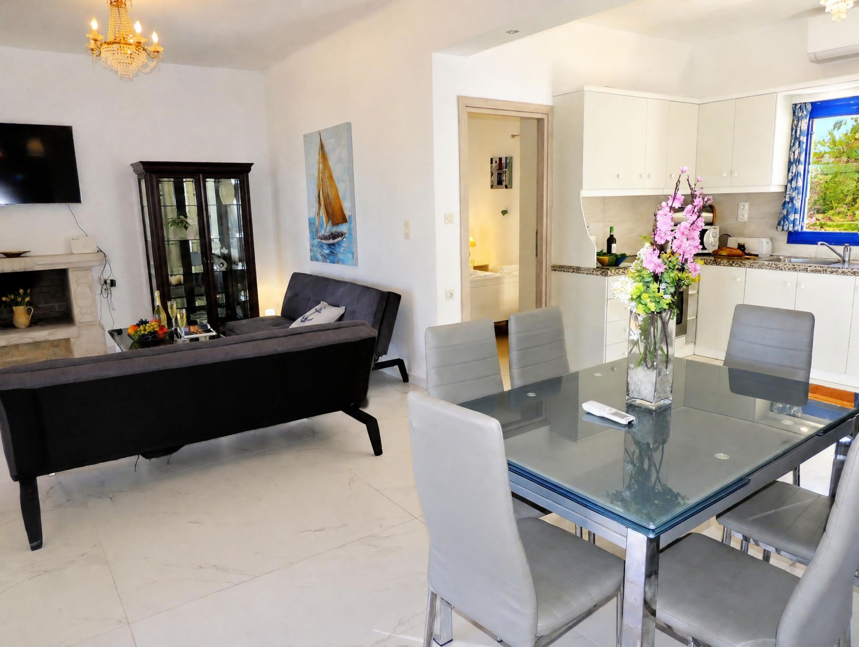 A modern living room with a glass-top dining table, grey sofas, and a fireplace.