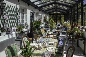 A conservatory with a glass roof, furnished with chairs and tables, surrounded by potted plants and flowers. - Villa marguerite charming bed and breakfast (Ponts-et-Marais)