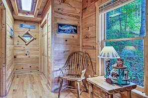 A wooden cabin interior with a wooden chair, a table with a lamp, and a window with a view of the forest. - Top Notch Fantastic Location Quiet, Seasonal Views (Gatlinburg)