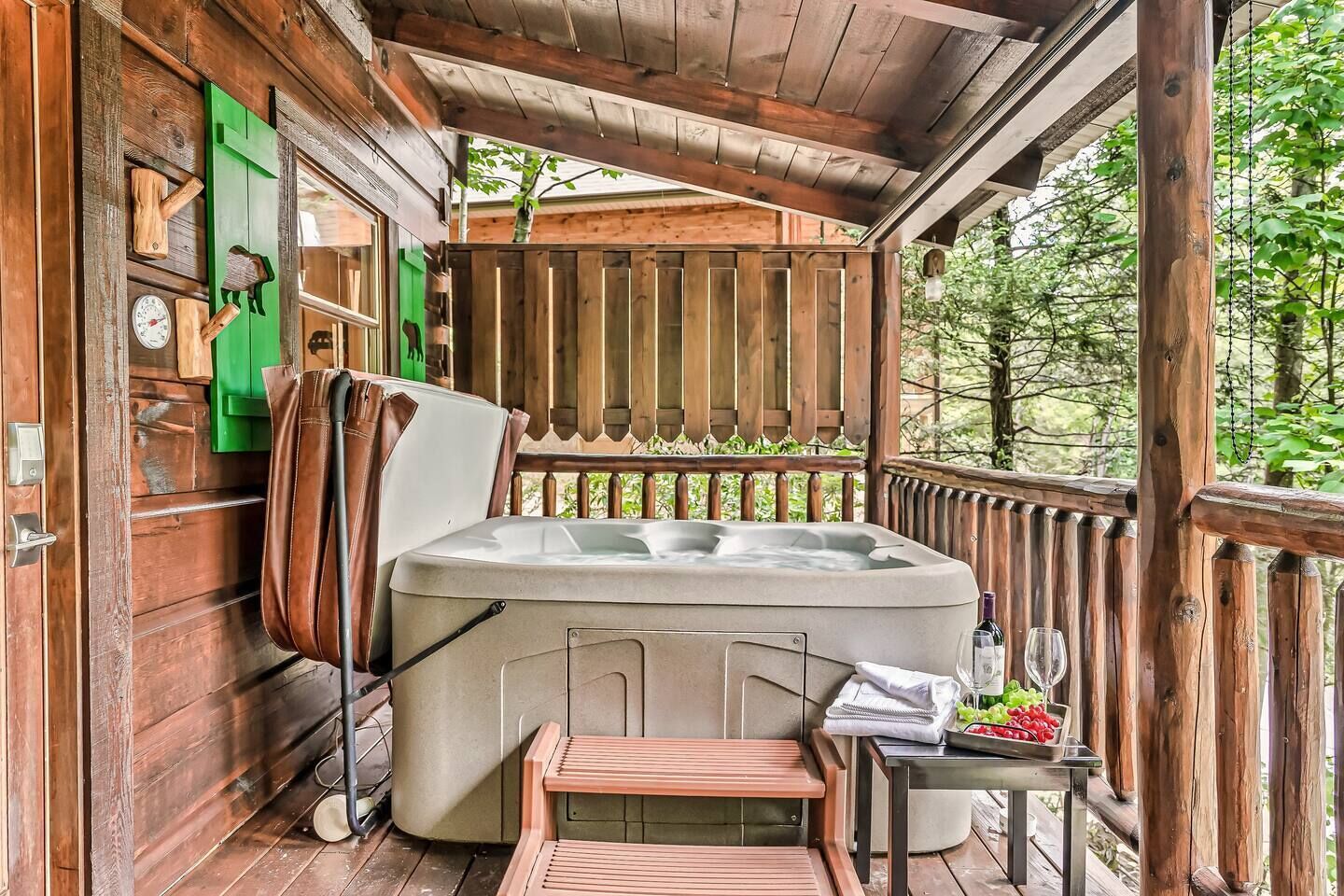 Une terrasse en bois avec un jacuzzi, un banc et une table sur laquelle se trouvent une bouteille et un verre.