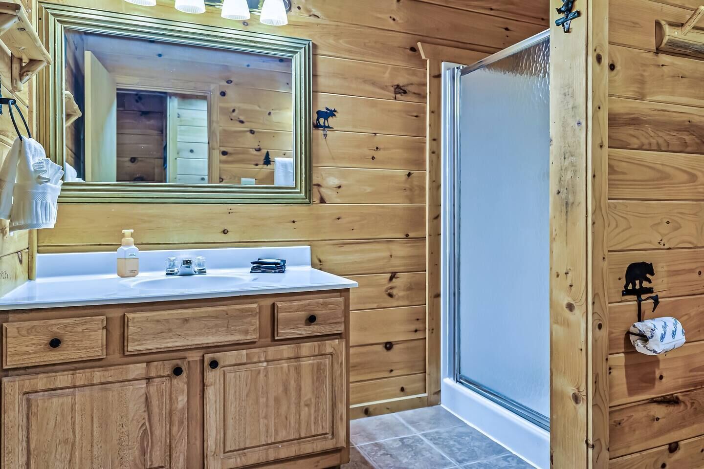 A wooden cabin bathroom with a wooden vanity, a mirror, a sink, and a shower area.