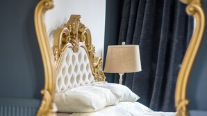 Una cama con cabecera dorada y una lámpara color beige a su lado.