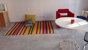 Een kamer met een kleurrijk gestreept tapijt, een rode stoel, een witte tafel en een kleine rode mok.