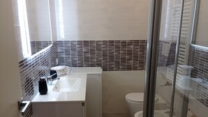 Een moderne badkamer met een douchecabine van glas, een witte wastafel en een toilet.