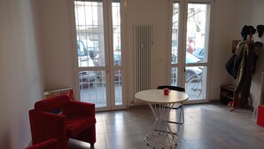 Een kamer met een witte tafel en stoelen, een rode bank, een radiator en uitzicht op geparkeerde auto's door een glazen deur.