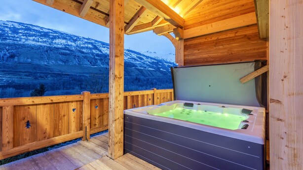 Una terraza de madera con un jacuzzi y vista a una montaña nevada.