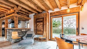 Un interior rústico con vigas de madera a la vista, pared de piedra, una puerta de madera grande y un comedor con mesa y sillas.