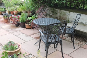 A patio with a round metal table and two chairs, surrounded by potted plants and a stone wall. - Number 48 - an apartment that sleeps 2 guests in 1 bedroom (Dumfries)