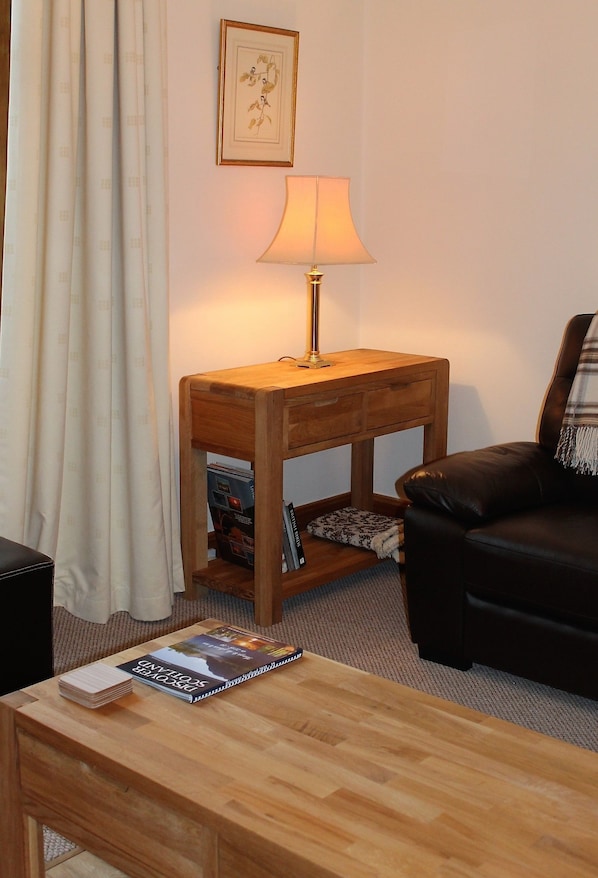 A cozy living room with a wooden side table, a lamp, a leather sofa, and a coffee table with a book.