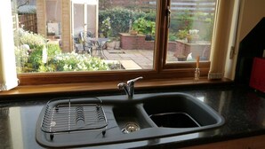 Una cucina con lavello, una finestra e vista su un giardino e un capanno.