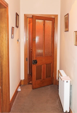 A hallway with a wooden door, a radiator, and framed pictures on the walls.