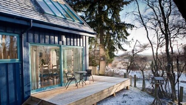 A wooden deck with outdoor seating, a glass door entrance, and a view of a snowy landscape.