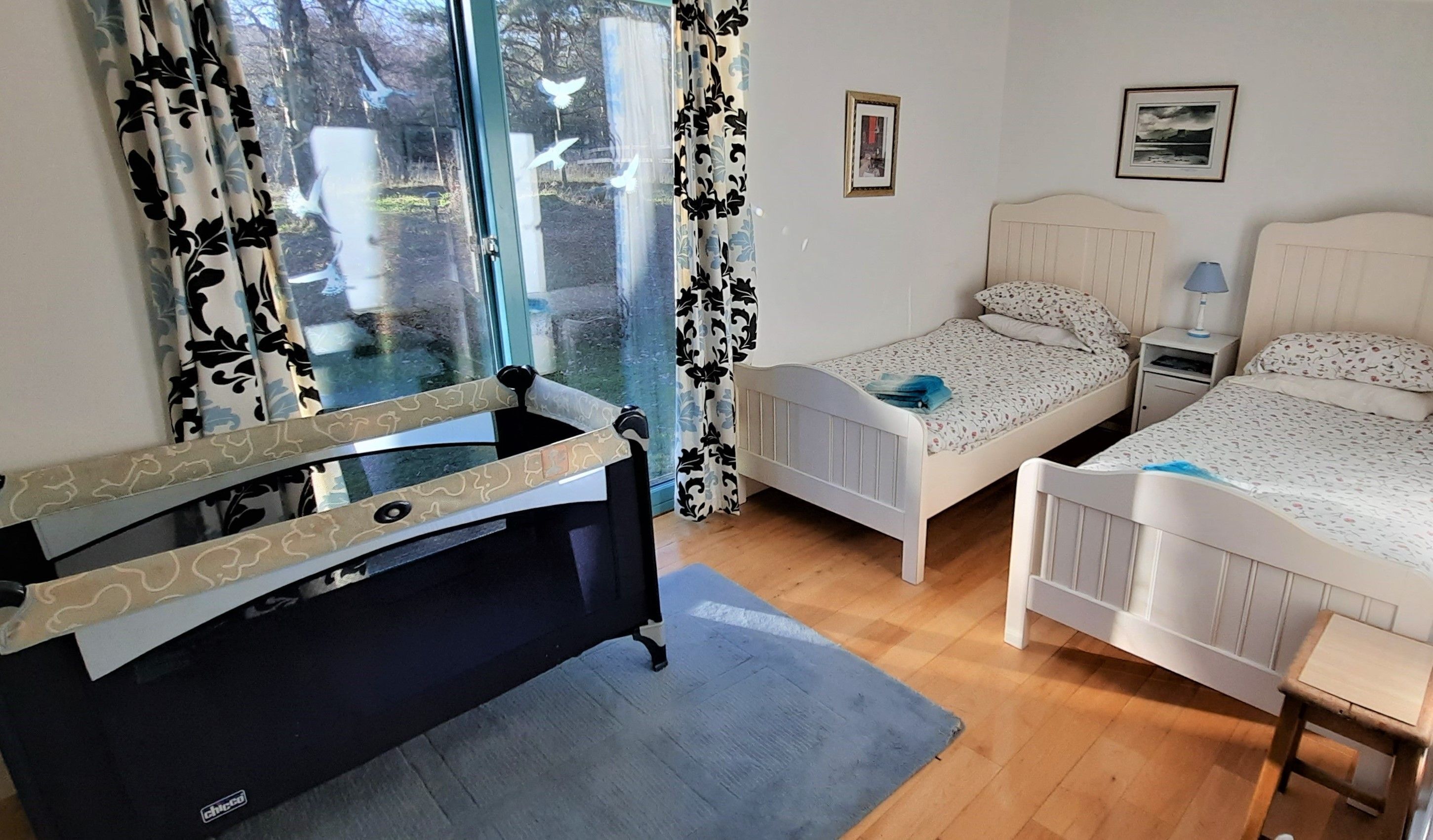 A bedroom with two single beds, a desk, and a large window with curtains.
