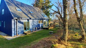 A blue house with a sloped roof, large windows, and a small deck.