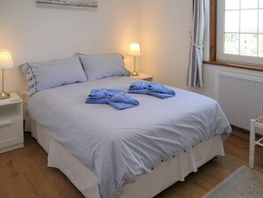 Un lit bien fait, avec une couvre-lit à rayures et des oreillers, une lampe de chevet et une vue sur l’extérieur par la fenêtre.