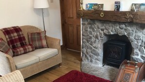 Un salon avec une cheminée en pierre, un canapé, un tapis rouge et une commode en bois.