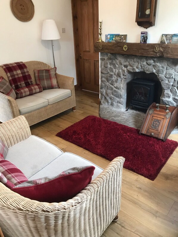 A living room with a stone fireplace, a sofa, a red rug, and a wooden chest. - Primrose Cottage -  a cottage that sleeps 4 guests  in 2 bedrooms (Rockcliffe)