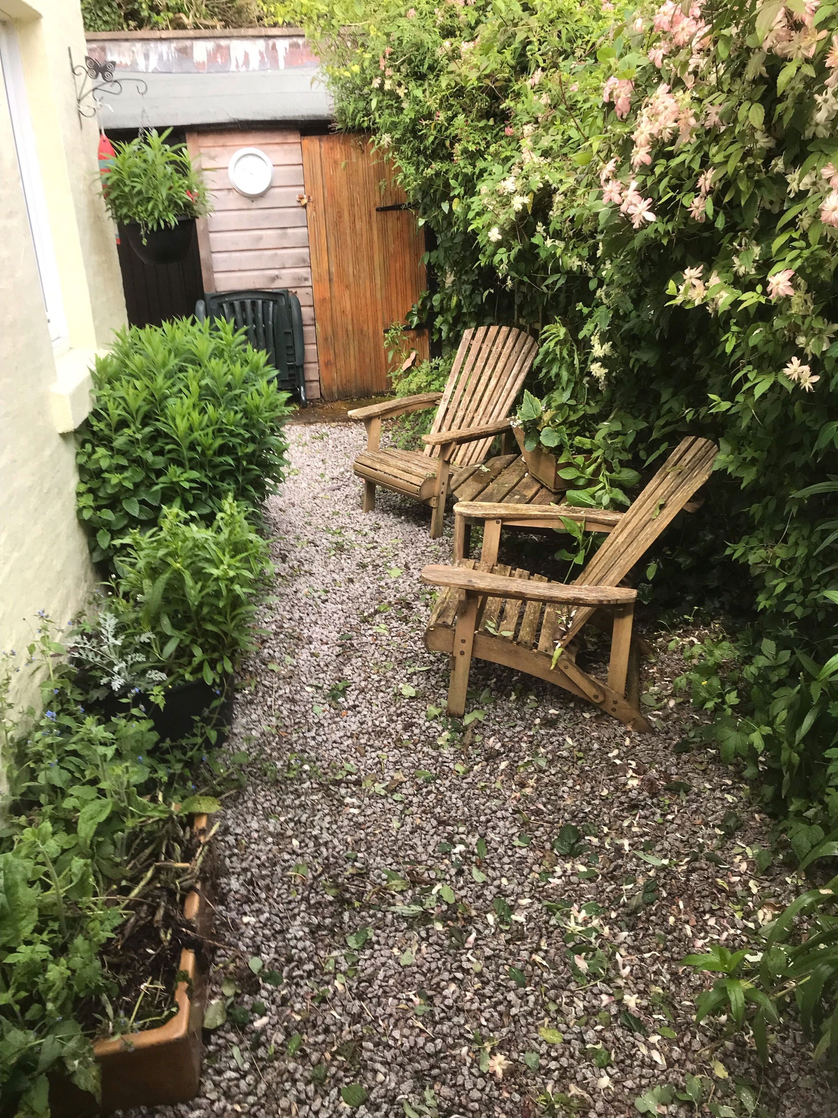 A garden with two wooden Adirondack chairs, a wooden fence, and various plants.