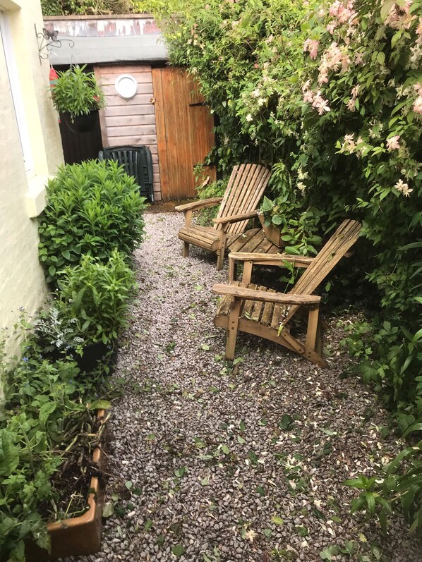 Een tuin met twee houten Adirondack stoelen, een houten hek en verschillende planten.
