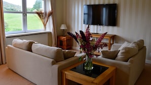 A living room with a sofa set, a coffee table, a TV, and a window with curtains. - Portling View -  an apartment that sleeps 6 guests  in 3 bedrooms (Dalbeattie)