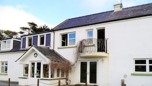 A white building with a dark roof, a balcony with a black railing, and a door with a glass panel. - Portling View -  an apartment that sleeps 6 guests  in 3 bedrooms (Dalbeattie)