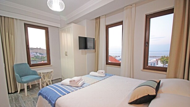 A hotel room with a bed, a chair, a small table, a TV, and a view of the sea. - Narlı Pansiyon (Bozcaada)