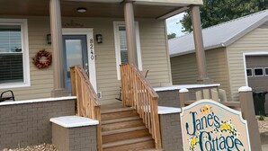 A two-story building with a front porch, a wooden staircase, and a sign for Jane's Cottage Retreat.