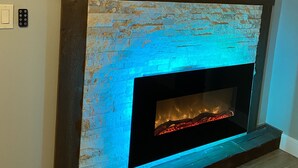 A fireplace with a blue-lit brick facade, a framed picture above it, and a light switch on the wall to the left.