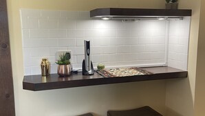A kitchen with white subway tiles, a dark countertop, two stools, and a small shelf with a plant.