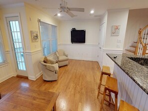 Enjoy a spacious living area with a kitchen, television, and staircase leading to an upper level.