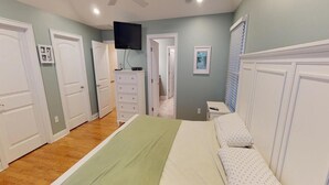 Een slaapkamer met een bed, een dressoir, een televisie en een deur naar een andere kamer.