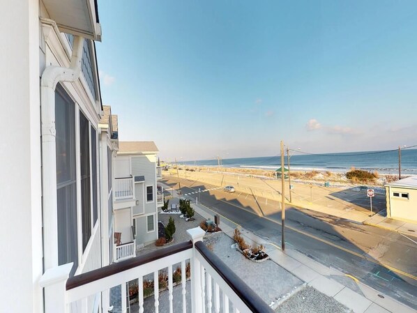 Enjoy the ocean views from this residential building's balcony overlooking a coastal street with a pedestrian walkway and sandy beach area.