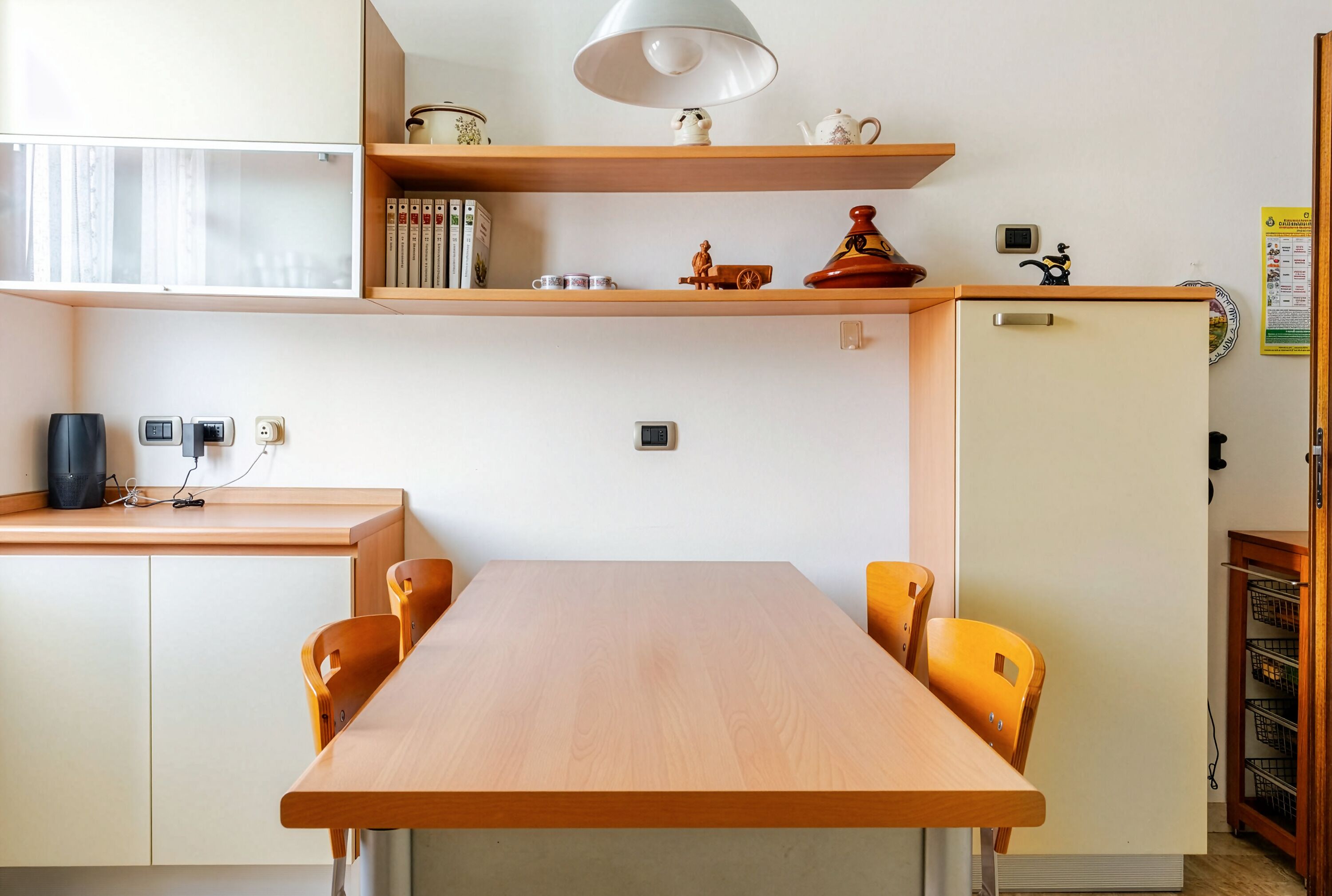 Un coin repas avec une table et des chaises en bois, une étagère avec des livres et des objets décoratifs, et un petit réfrigérateur.