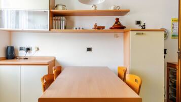 Un coin repas avec une table et des chaises en bois, une étagère avec des livres et des objets décoratifs, et un petit réfrigérateur.