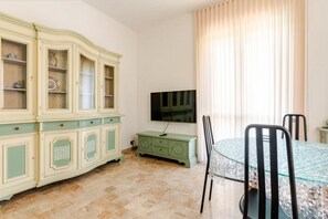 A room with a dining table, chairs, a television, and a cabinet with glass doors.
