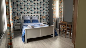 A bedroom with a patterned wall, a bed with blue bedding, a wooden chair, and a small table. - the house of the end of the world (Porspoder)