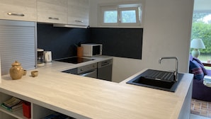 A modern kitchen with a light wood countertop, a built-in oven, a microwave, a sink, and a window above the countertop. - the house of the end of the world (Porspoder)