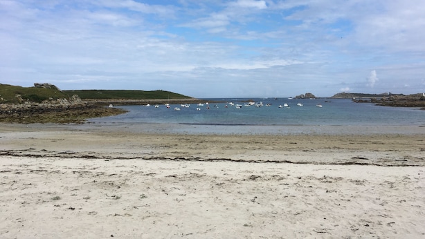 A beach with boats in the water and rocky hills in the background. - the house of the end of the world (Porspoder)