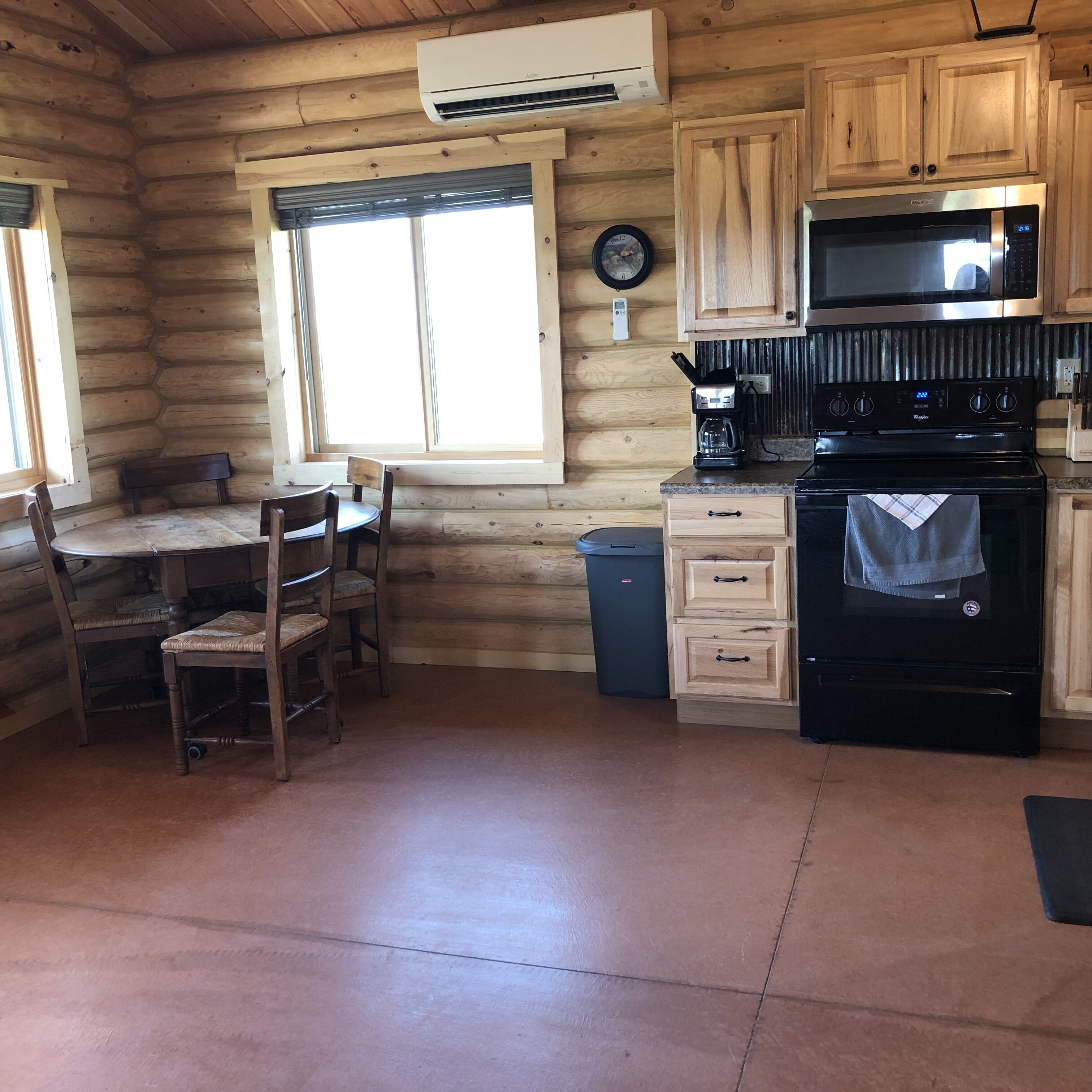 A log cabin interior with a kitchen area featuring a stove, microwave, and wooden cabinets.