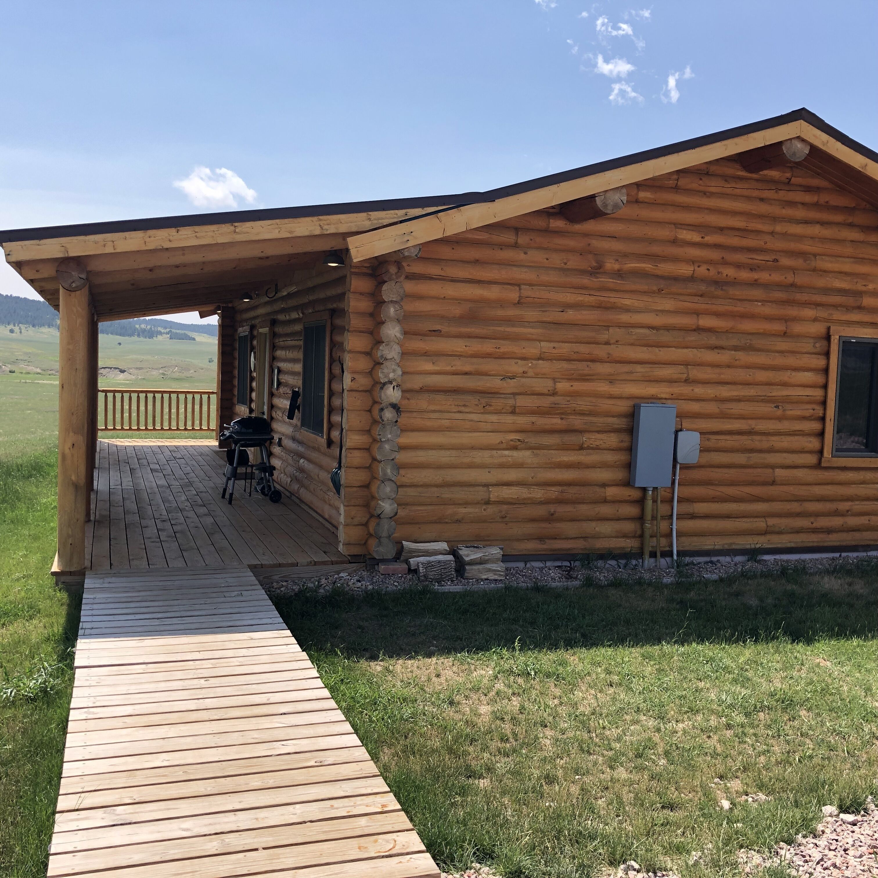 Una cabaña de troncos con porche cubierto, una silla de ruedas y vistas del paisaje circundante.