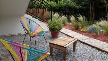 A patio with two colorful chairs, a small wooden table, and a potted plant.