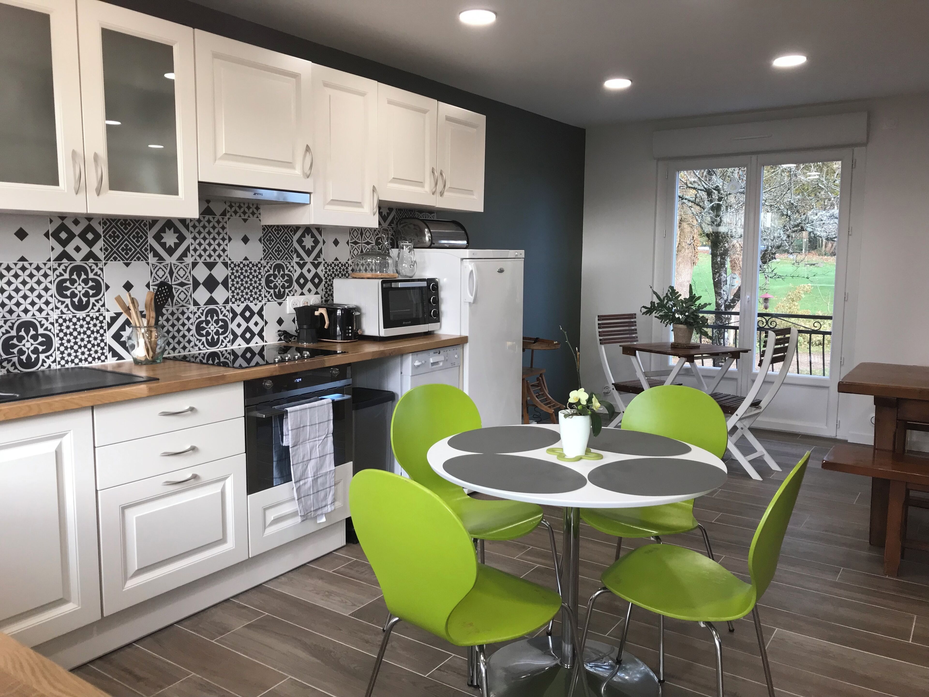 A modern kitchen with white cabinets, a microwave, and a coffee maker. There is a dining area with a round table and green chairs.