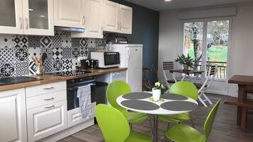 A modern kitchen with white cabinets, a microwave, and a coffee maker. There is a dining area with a round table and green chairs.